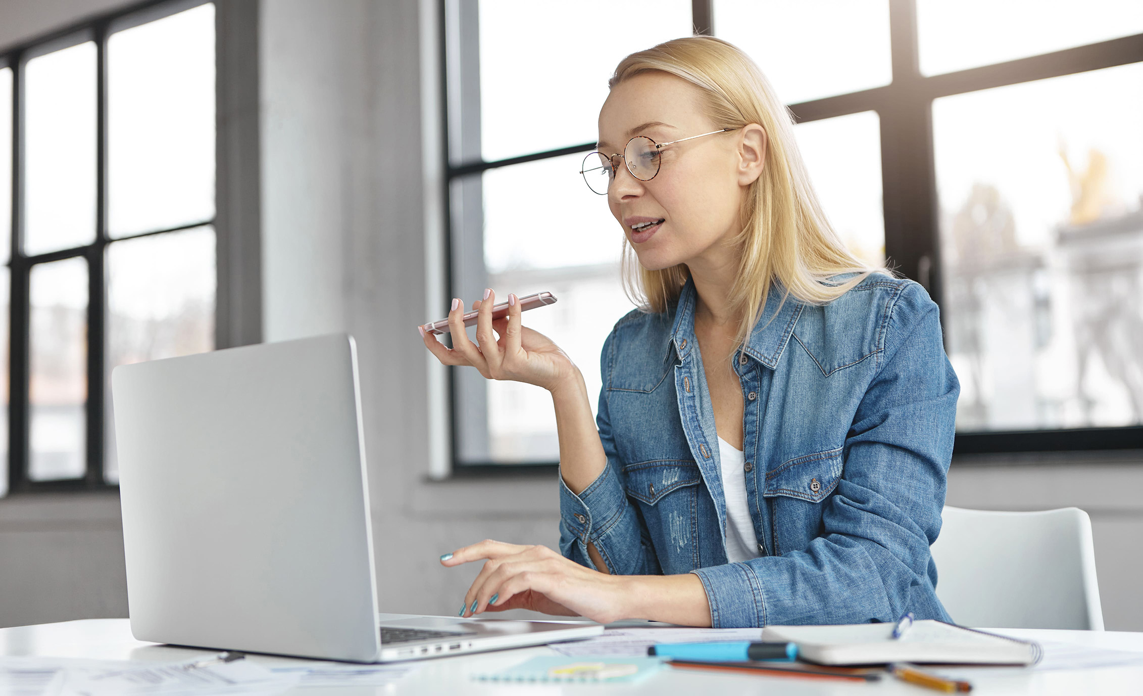 Frau, sitzend vor dem Laptop am telefonieren.